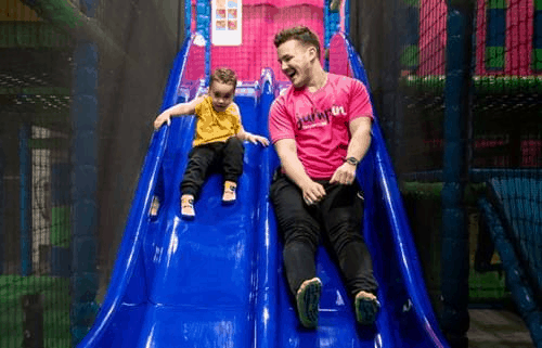 Jump In staff member sliding down a slide with a young child