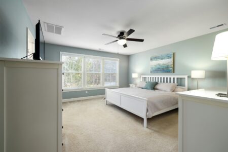 a minimalist white themed bedroom with large windows and a ceiling fan depicting a bedroom to help sleep in the heat.