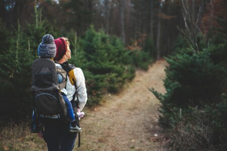 a woman with a young child in a hiking carrier walkign through woodlands