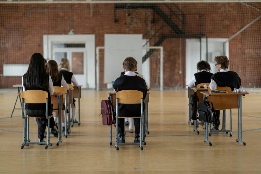 pexels-cottonbro-7395893 Rear view of students seated in a classroom, focusing on the backs of their heads and desks