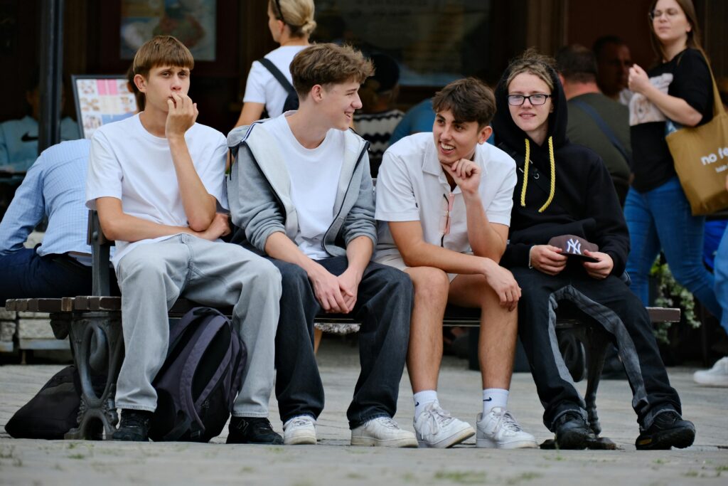 pexels-szafran-33265473 A group of relaxed teenage friends sitting together on a city bench, chatting and laughing in casual outfits.