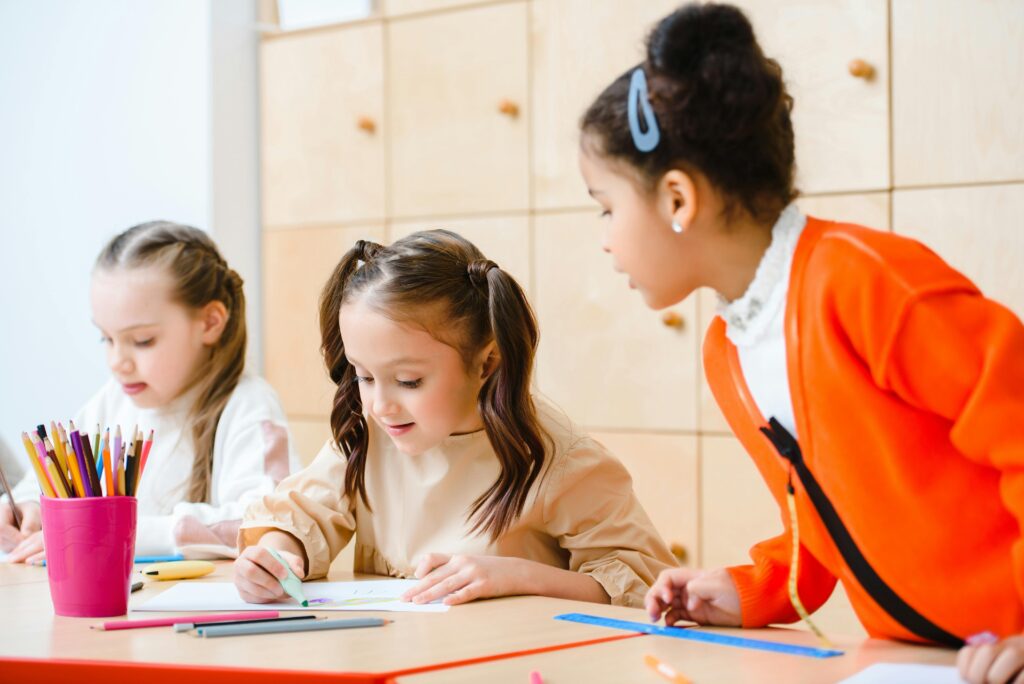 “Primary school children sitting together in a classroom, engaged in learning activities with books and school supplies