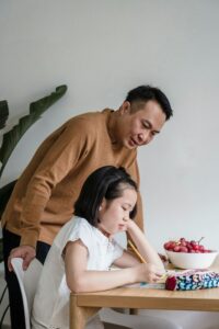 A young girl sitting at a table looking thoughtful, suggesting reflection and emotional awareness.