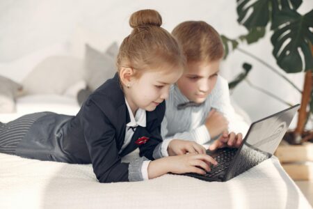 Two children in formal outfits working together at a laptop, collaborating on digital tasks indoors