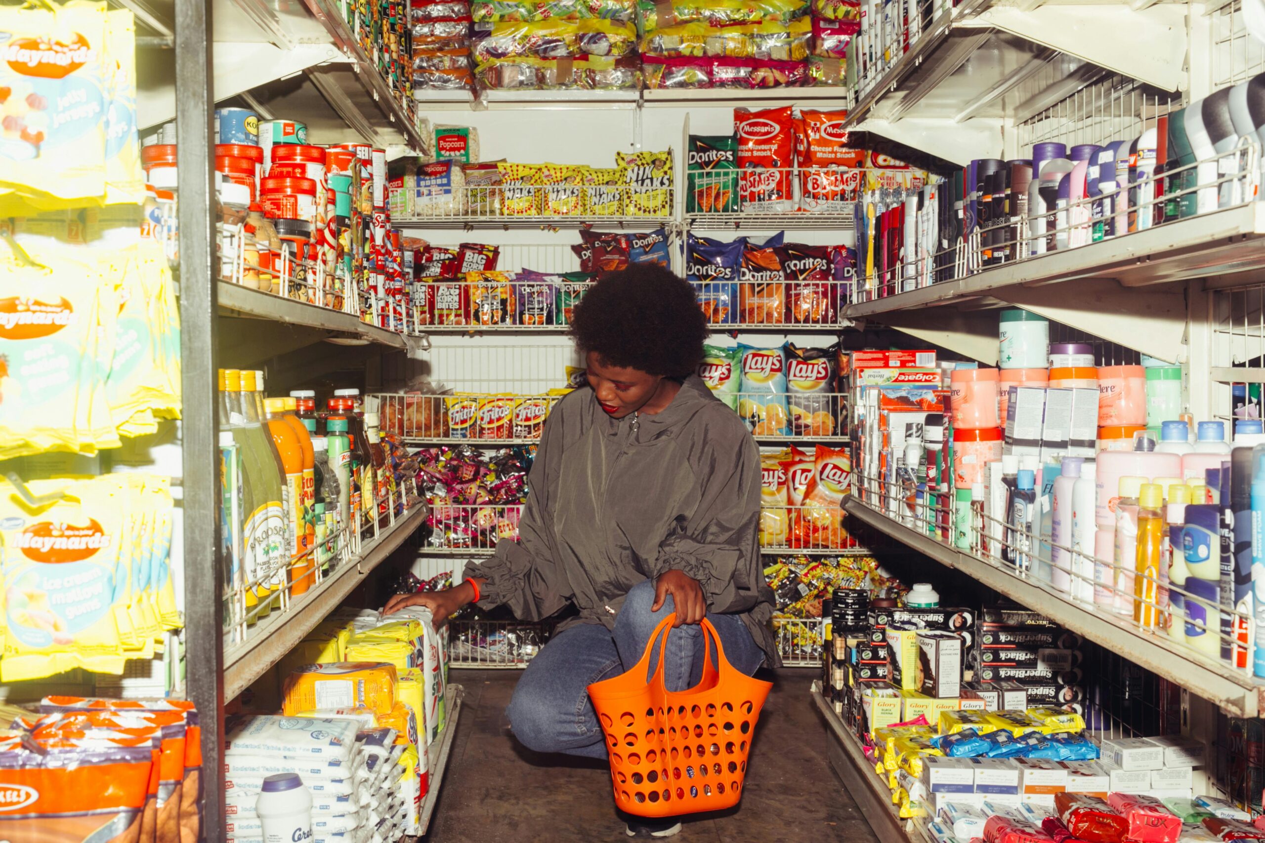 Woman selecting groceries in a shop aisle with a trolley, choosing food items thoughtfully