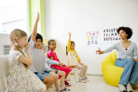 teacher leading a classroom lesson with children raising their hands to participate